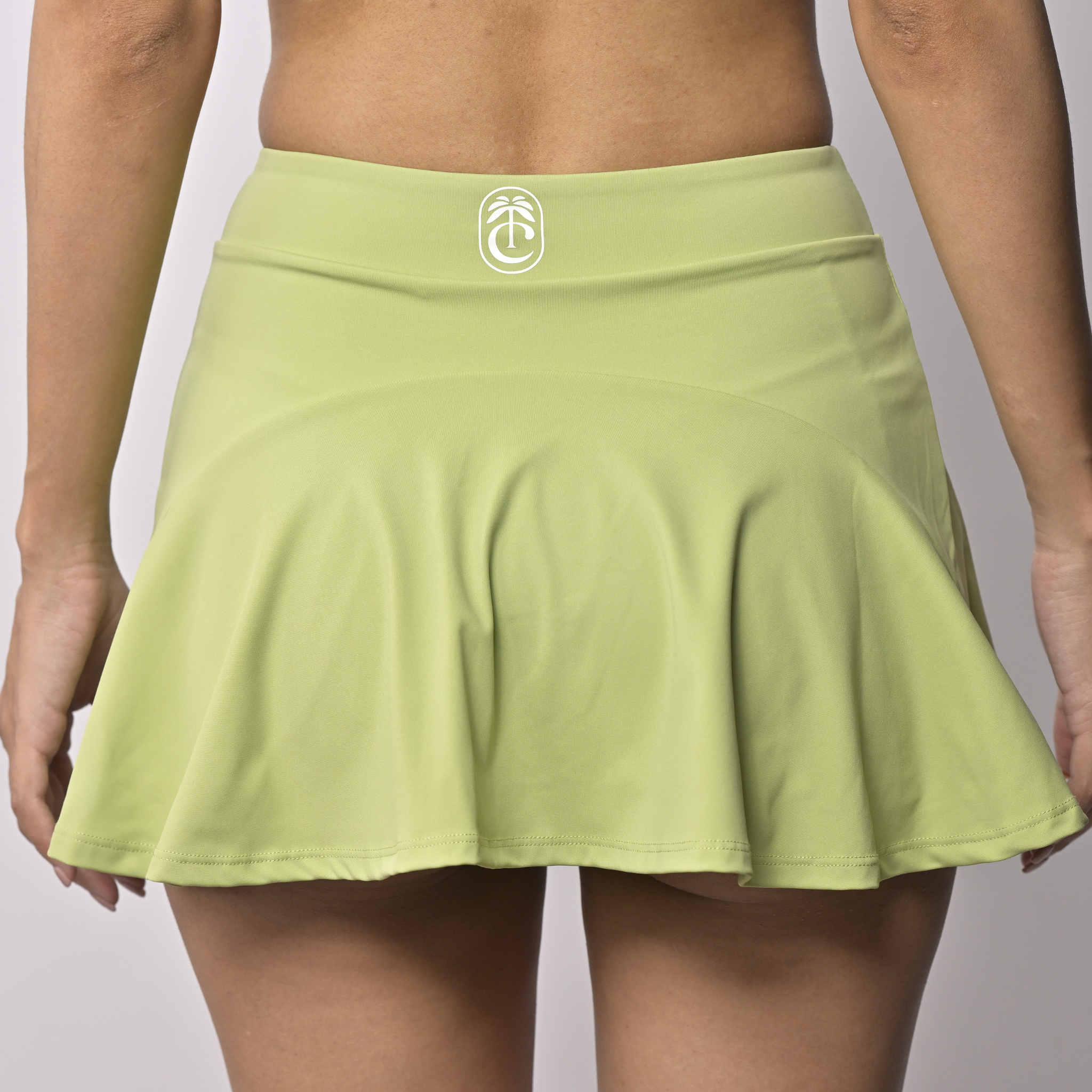 back view of Light green sports skort with a club tropikai logo in white  