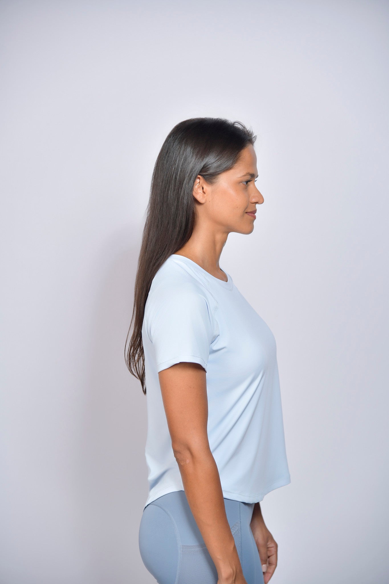 Woman wearing a light blue sports t-shirt and gray leggings against a white background