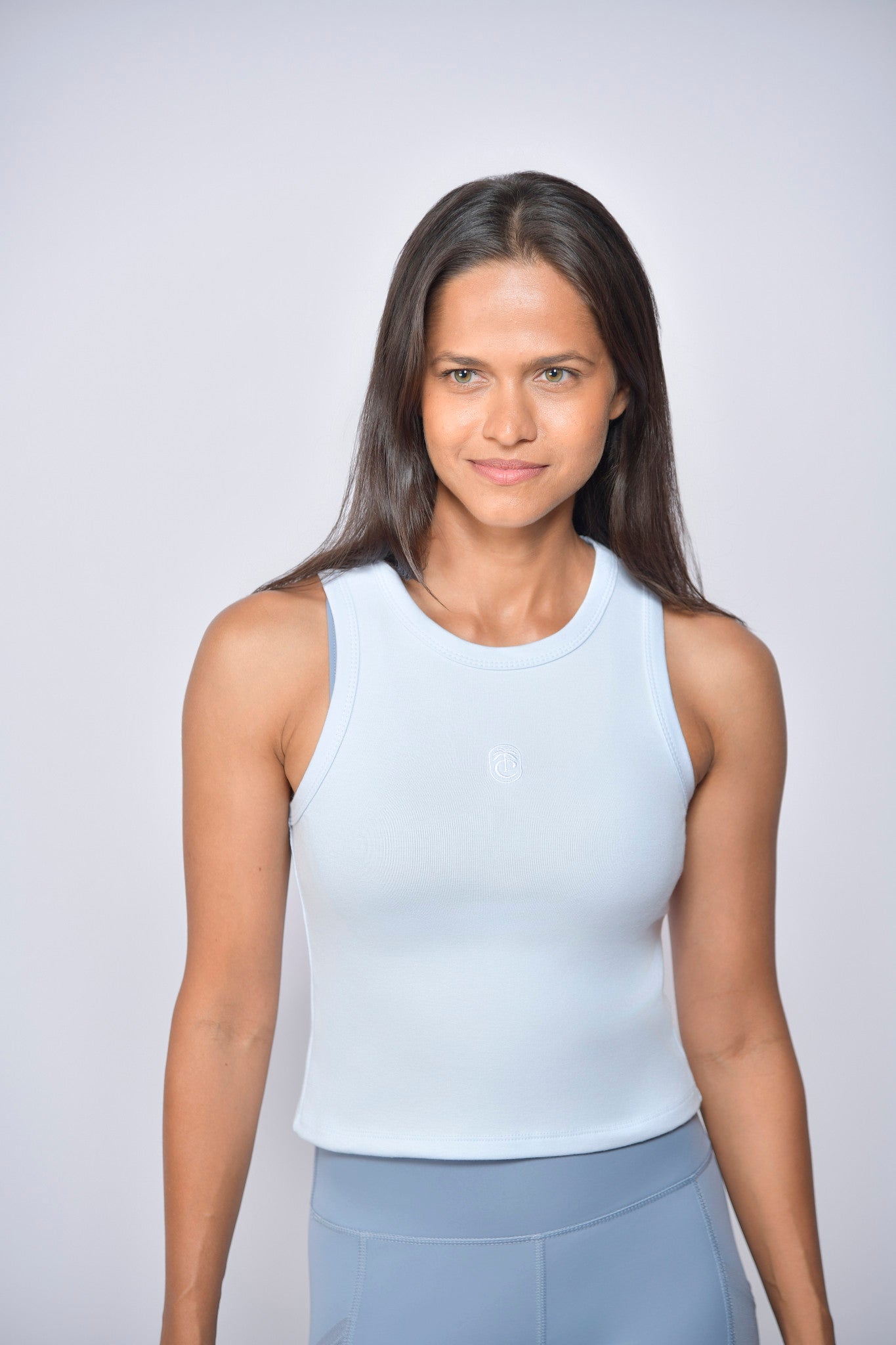 Woman wearing a baby blue sleeveless top and blue sports tights against a plain background