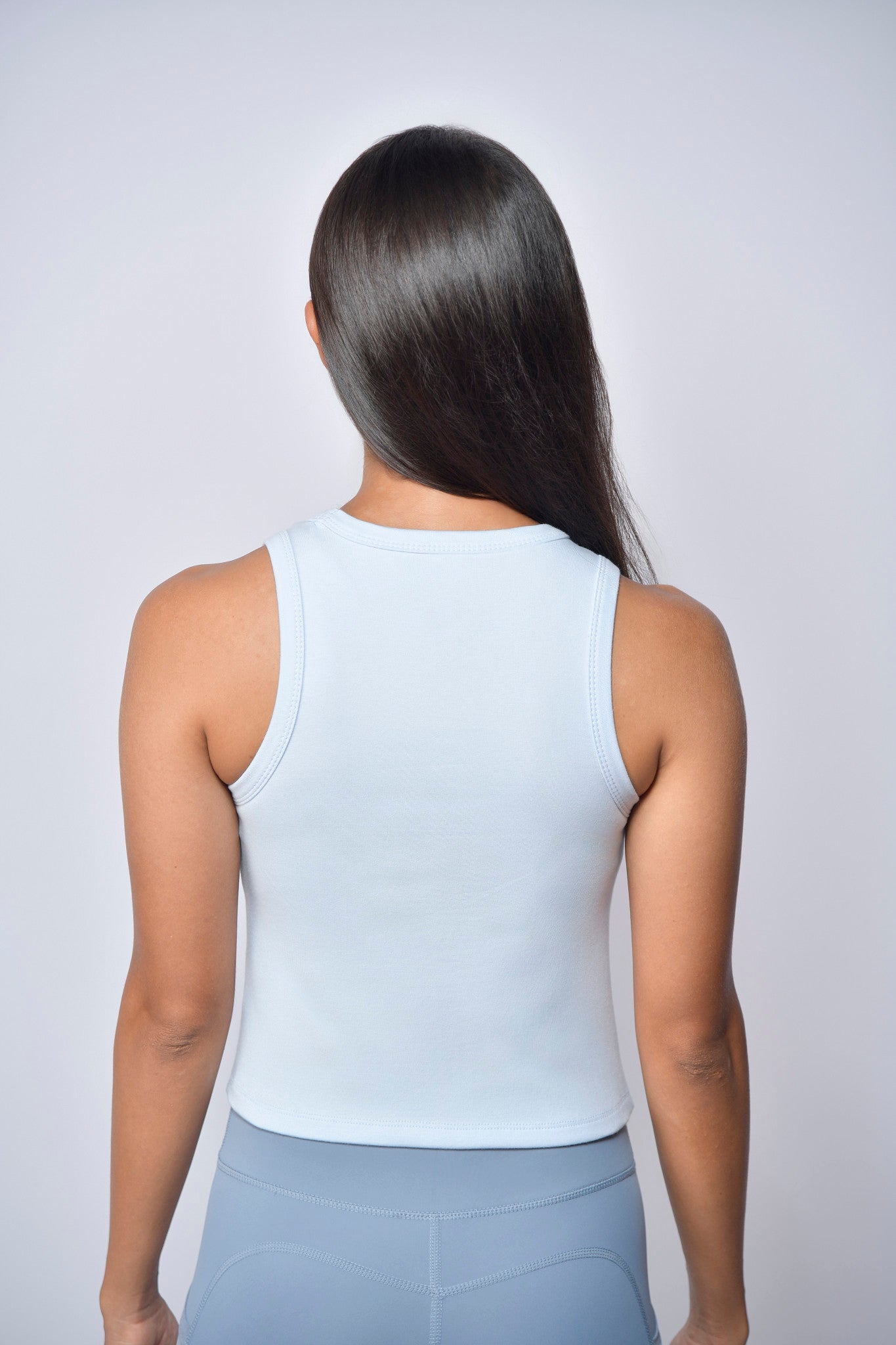 Person wearing a Light blue tank top and blue pants on a plain background