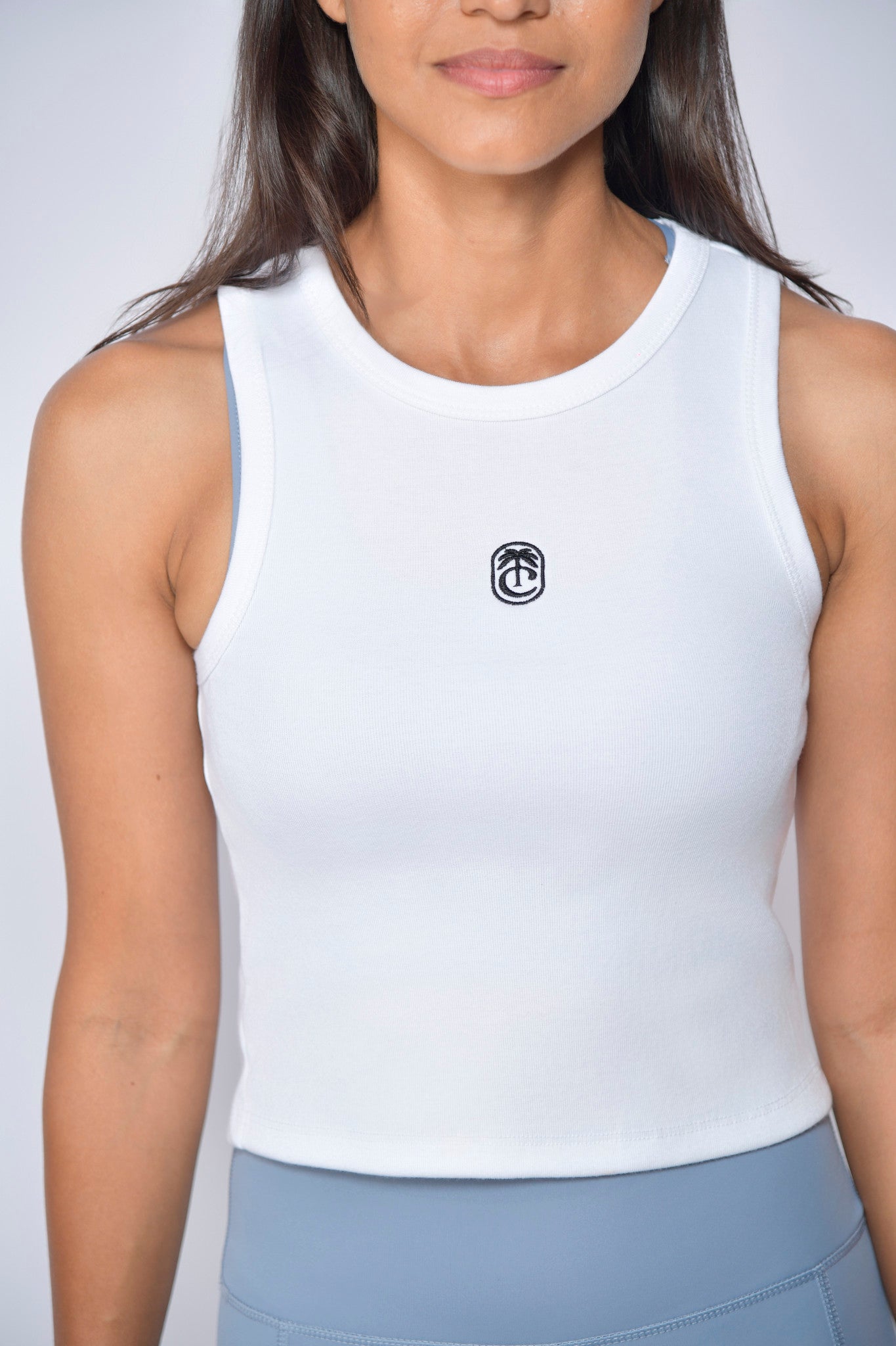Person wearing a white tank top with Club Tropikai logo  on a plain background