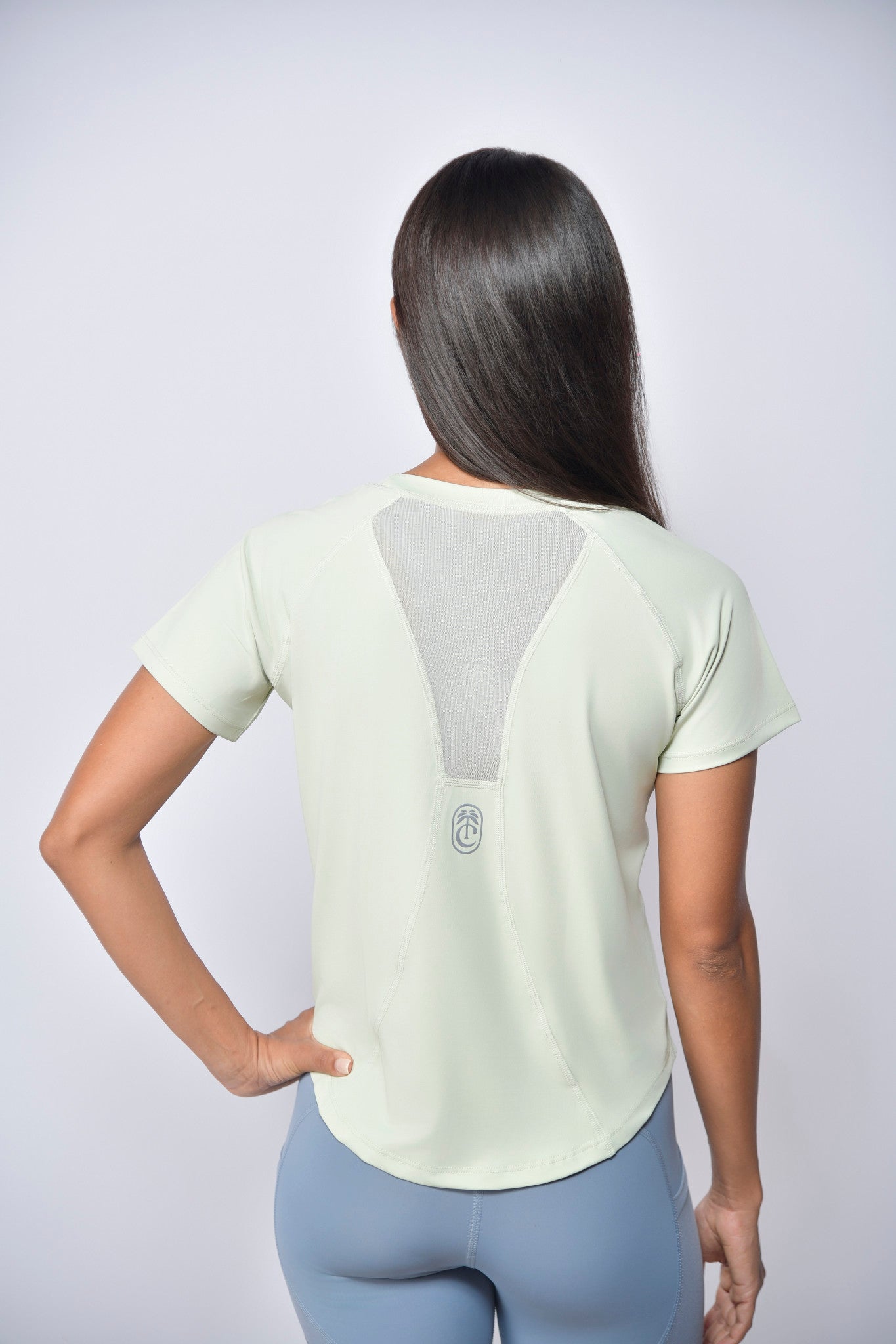 Woman wearing a light-colored t-shirt with  reflective club tropikai on the back against a plain background