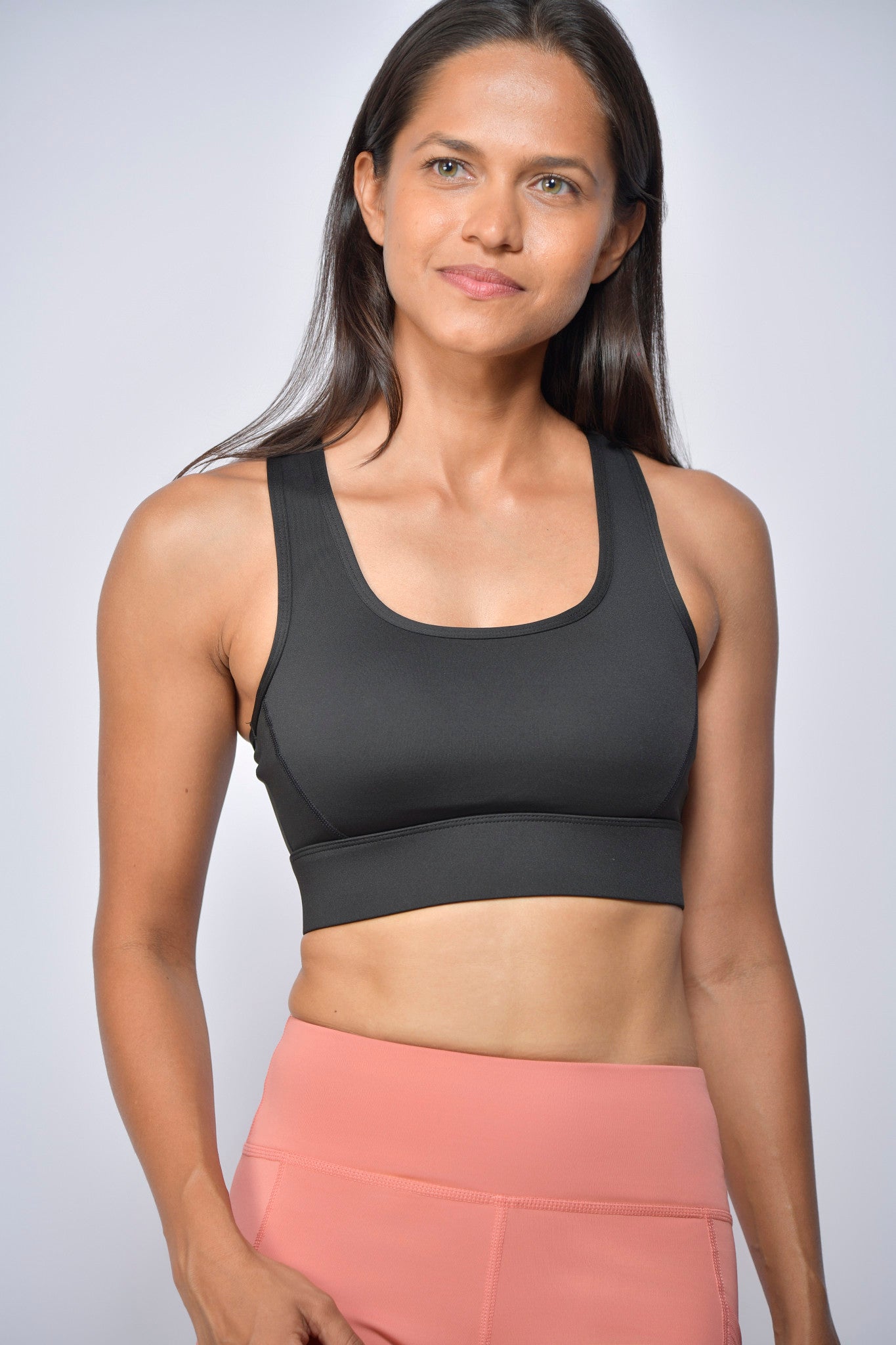 Woman wearing a black sports bra and pink leggings against a white background