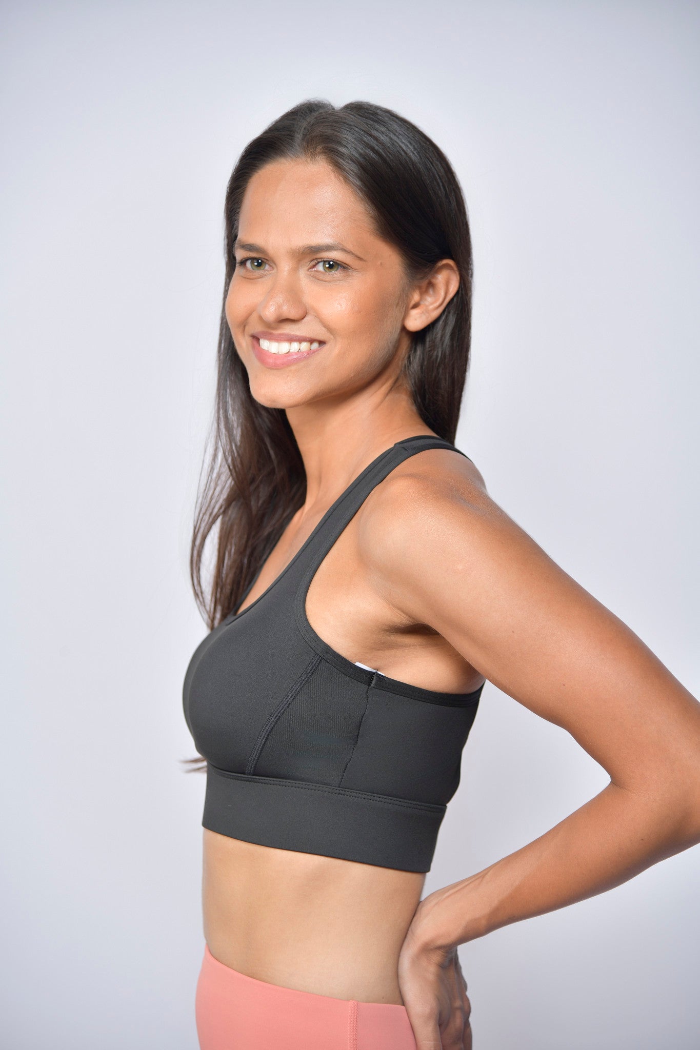 Woman wearing a black sports bra and pink pants against a light gray background