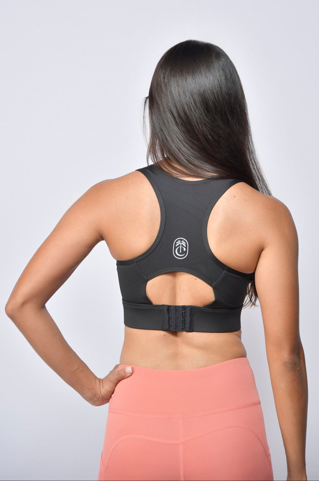 Woman wearing a black sports bra and pink leggings on a light gray background