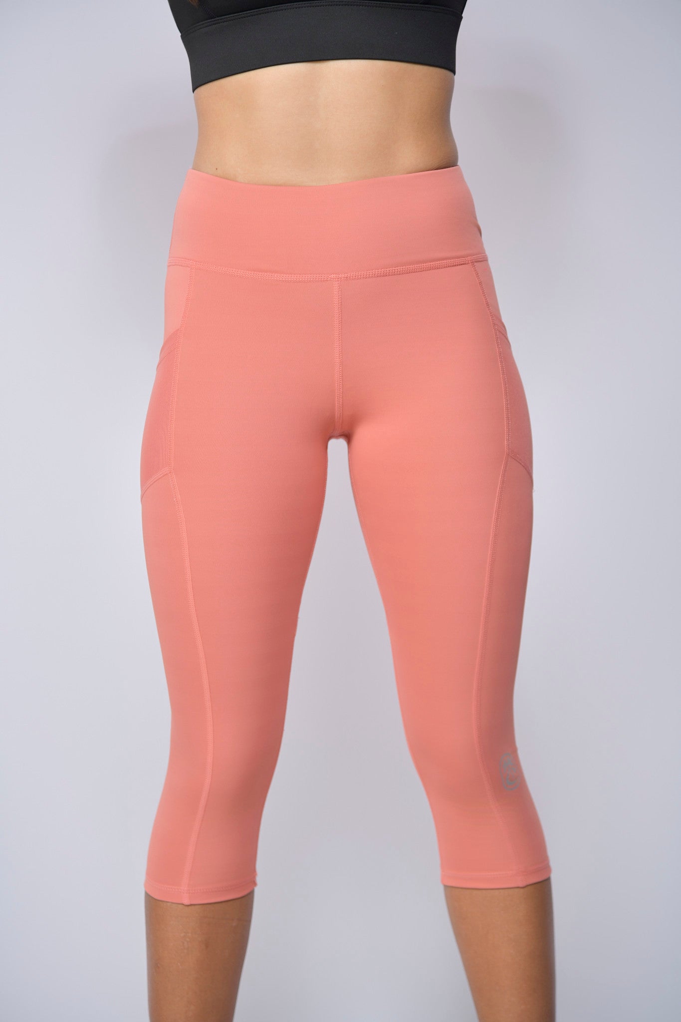 Peach-colored capri length leggings worn by a lady on a light gray background