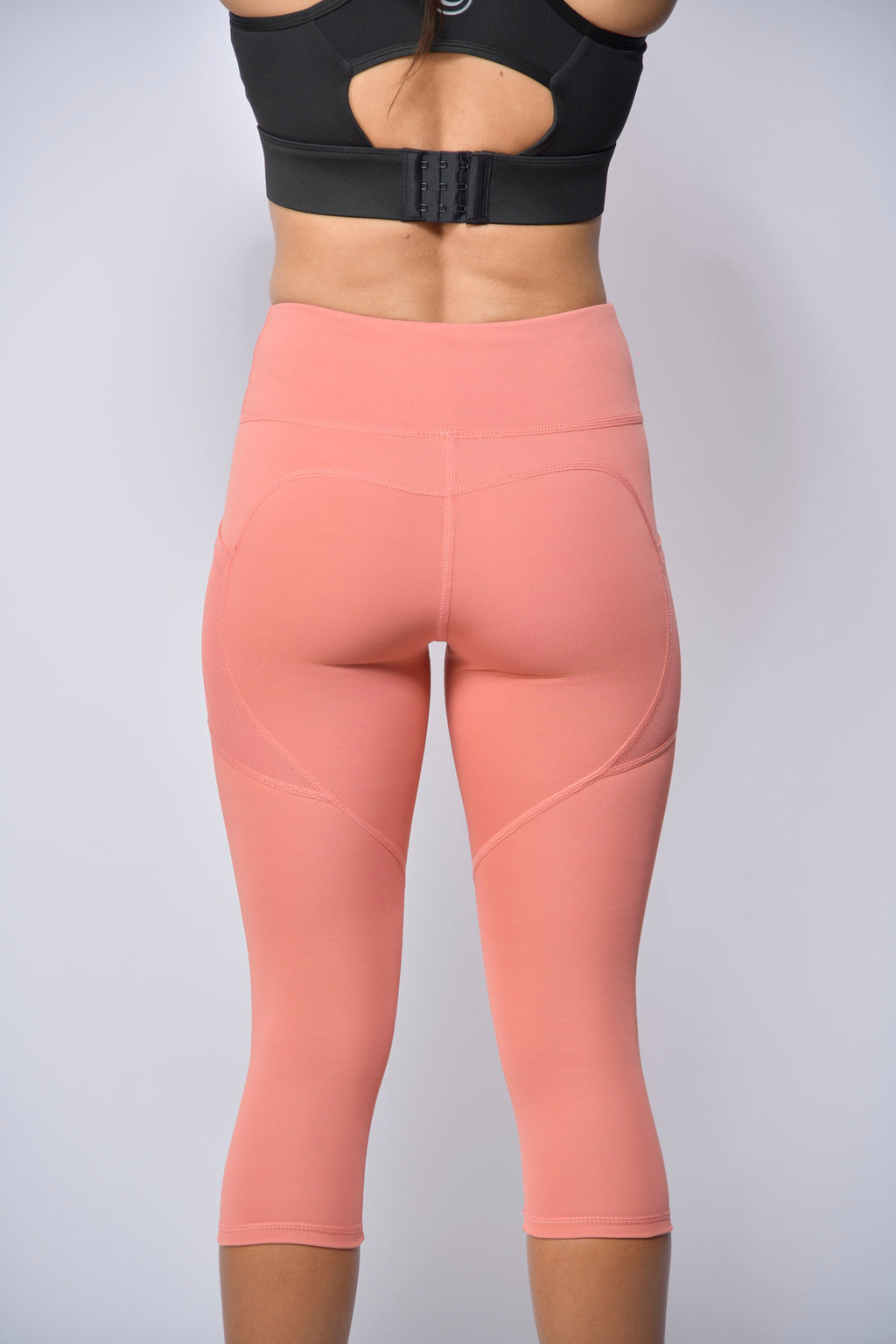 woman wearing peach leggings and black sports bra on a light gray background