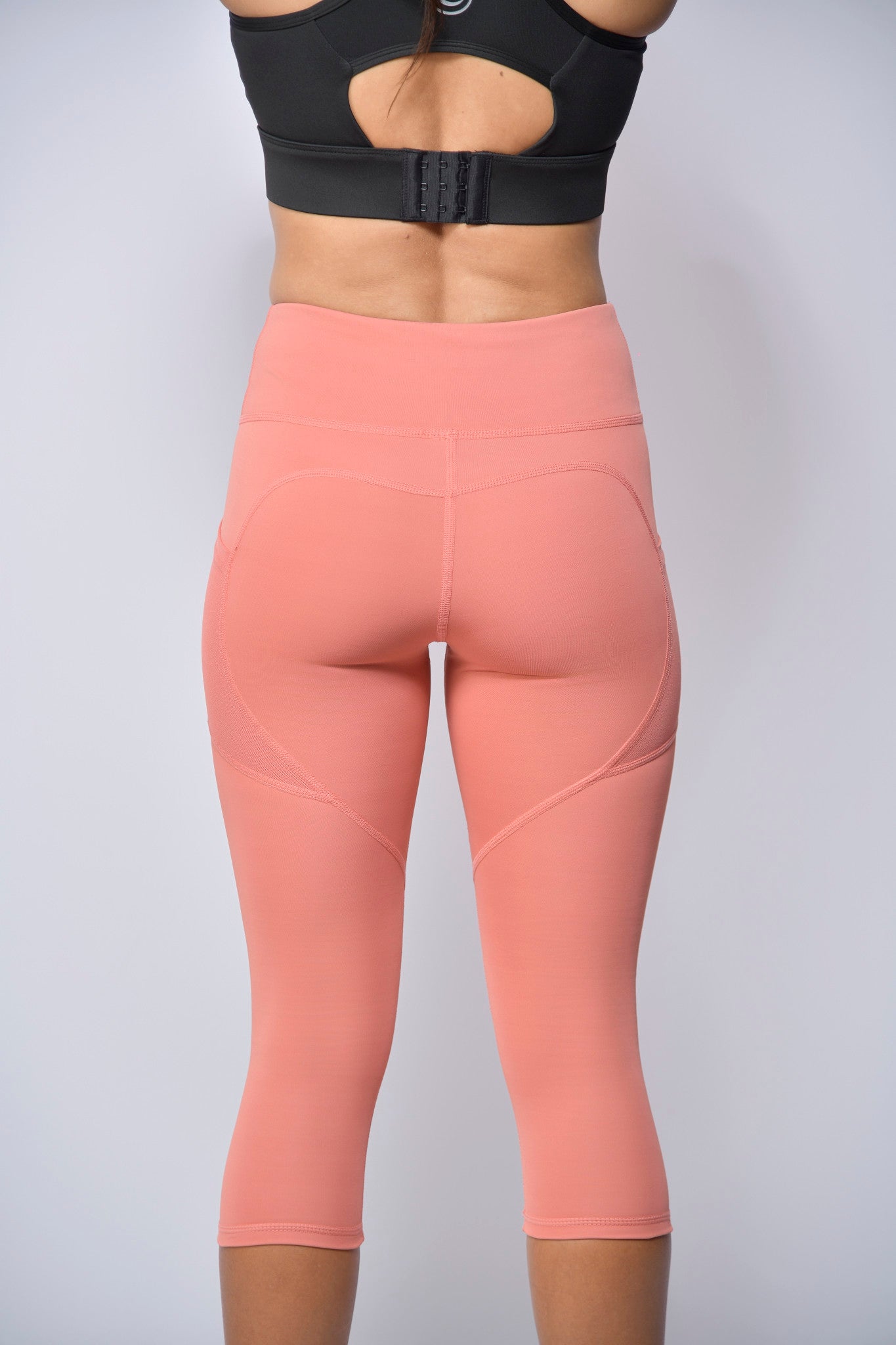 woman wearing peach leggings and black sports bra on a light gray background