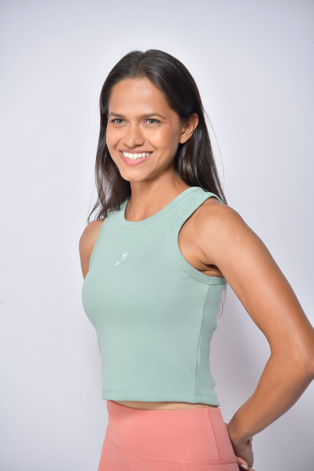 Woman wearing a light green tank top and peach tights against a white background