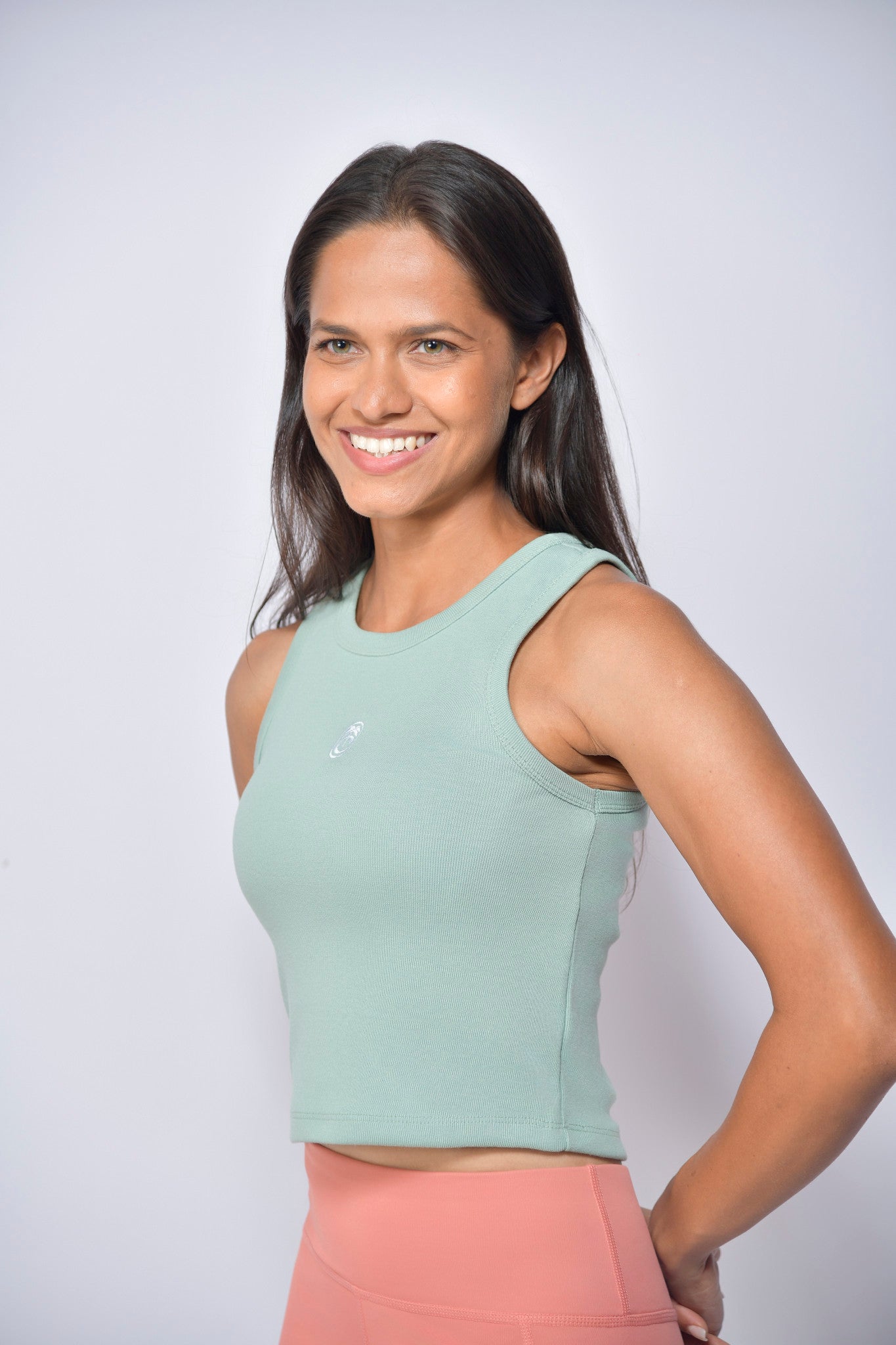 Woman wearing a light green tank top and peach tights against a white background