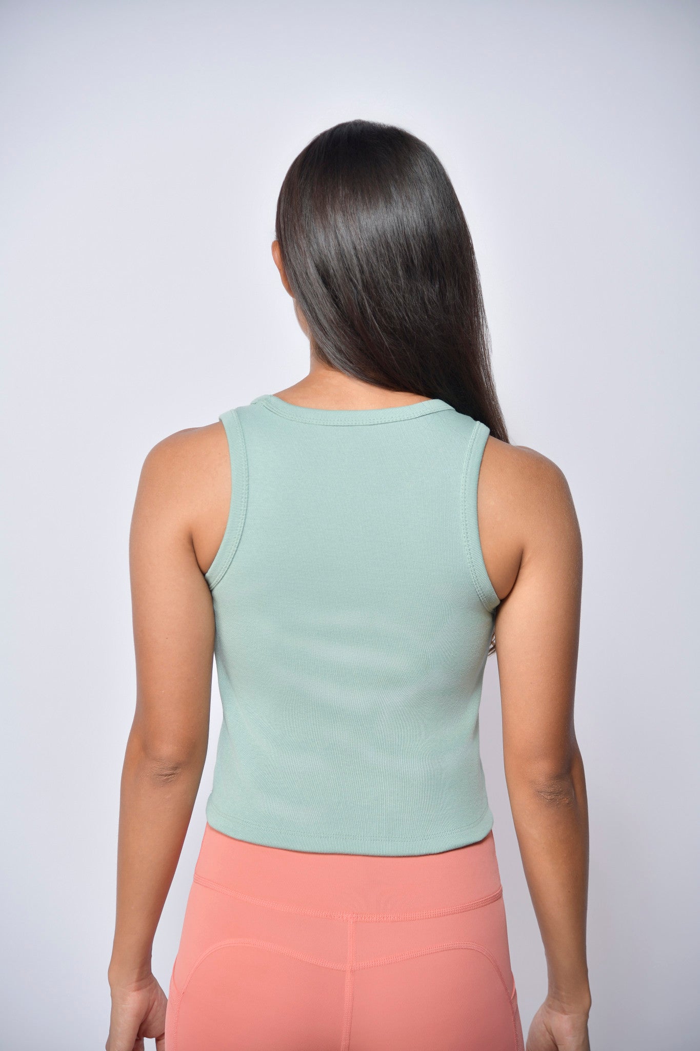Woman wearing a light green sleeveless top and peach tights against a white background