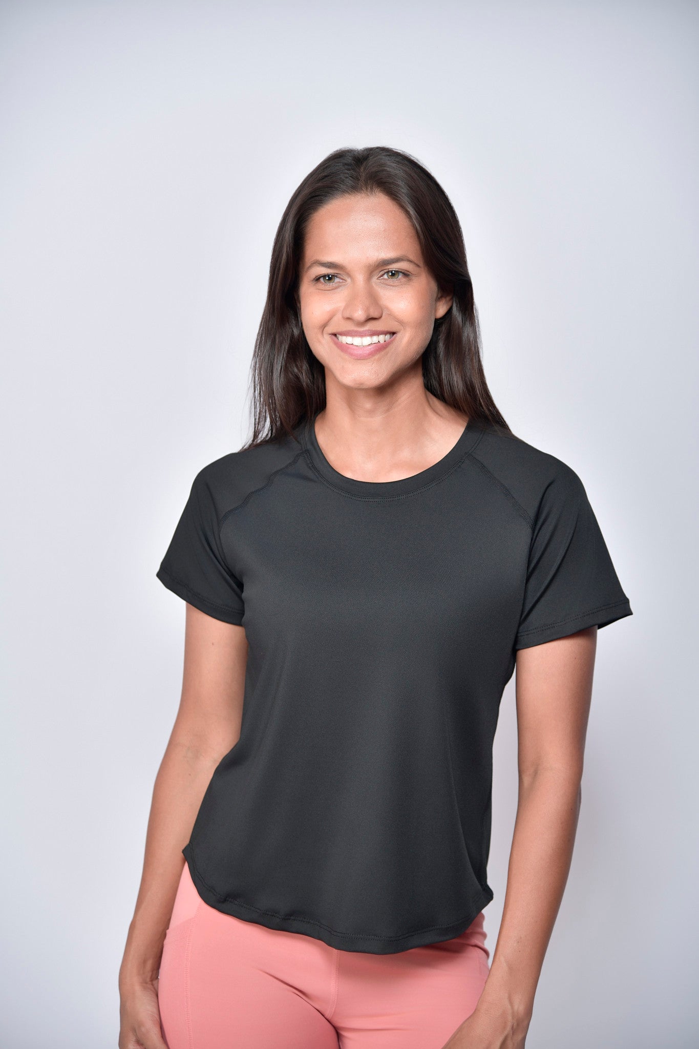 Woman wearing a black sports t-shirt with  reflective club tropikai on the back against a plain background
