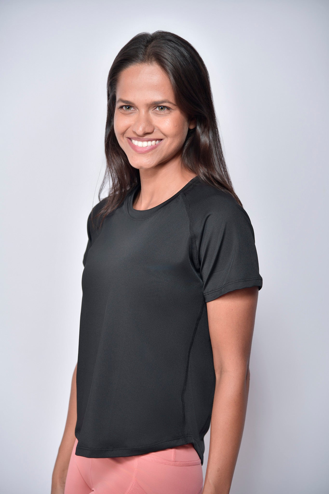 Woman wearing a black sports t-shirt with  reflective club tropikai on the back against a plain background
