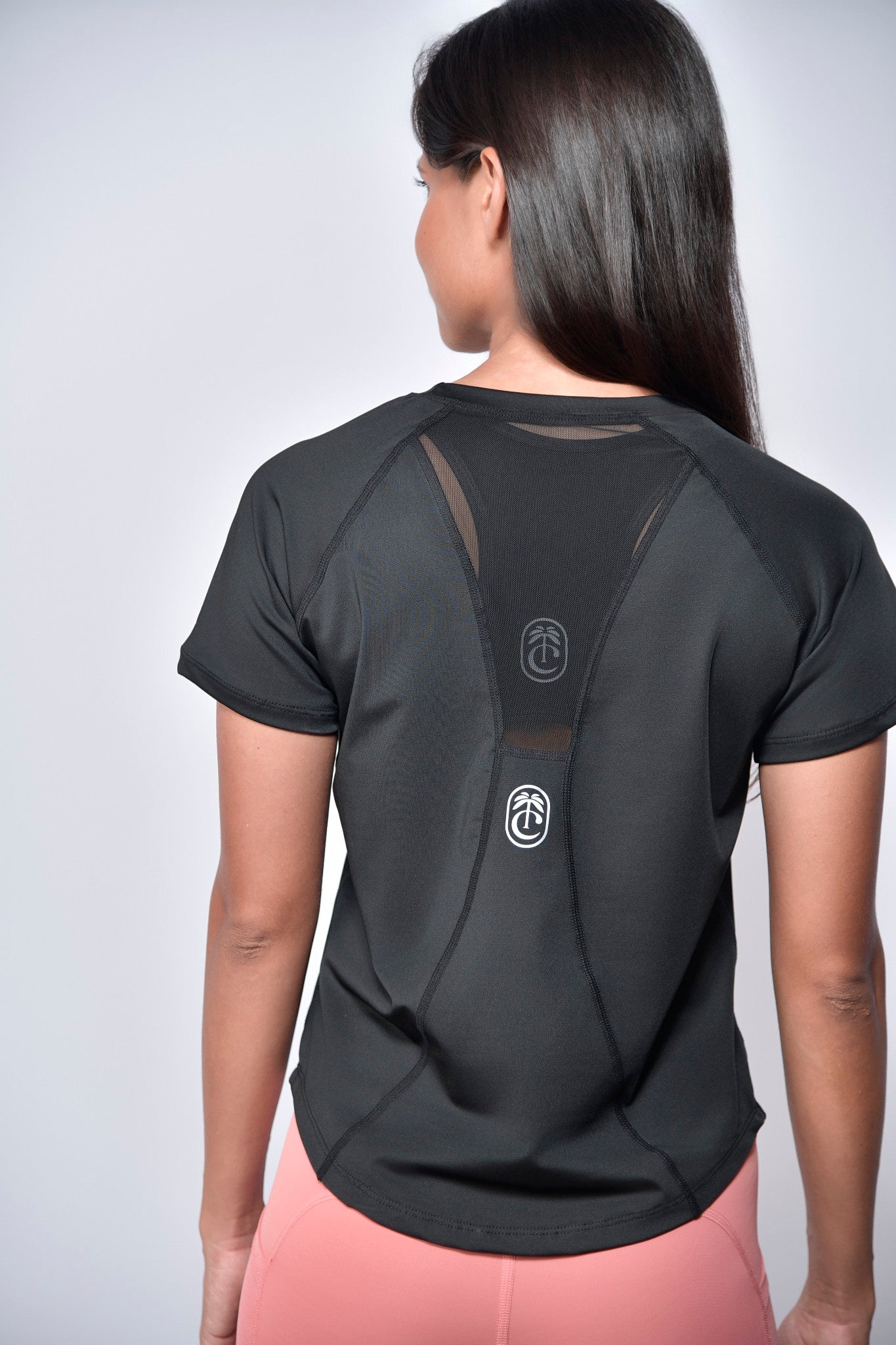 Person wearing a black athletic shirt with mesh panels  reflective club tropikai on the back against a plain background